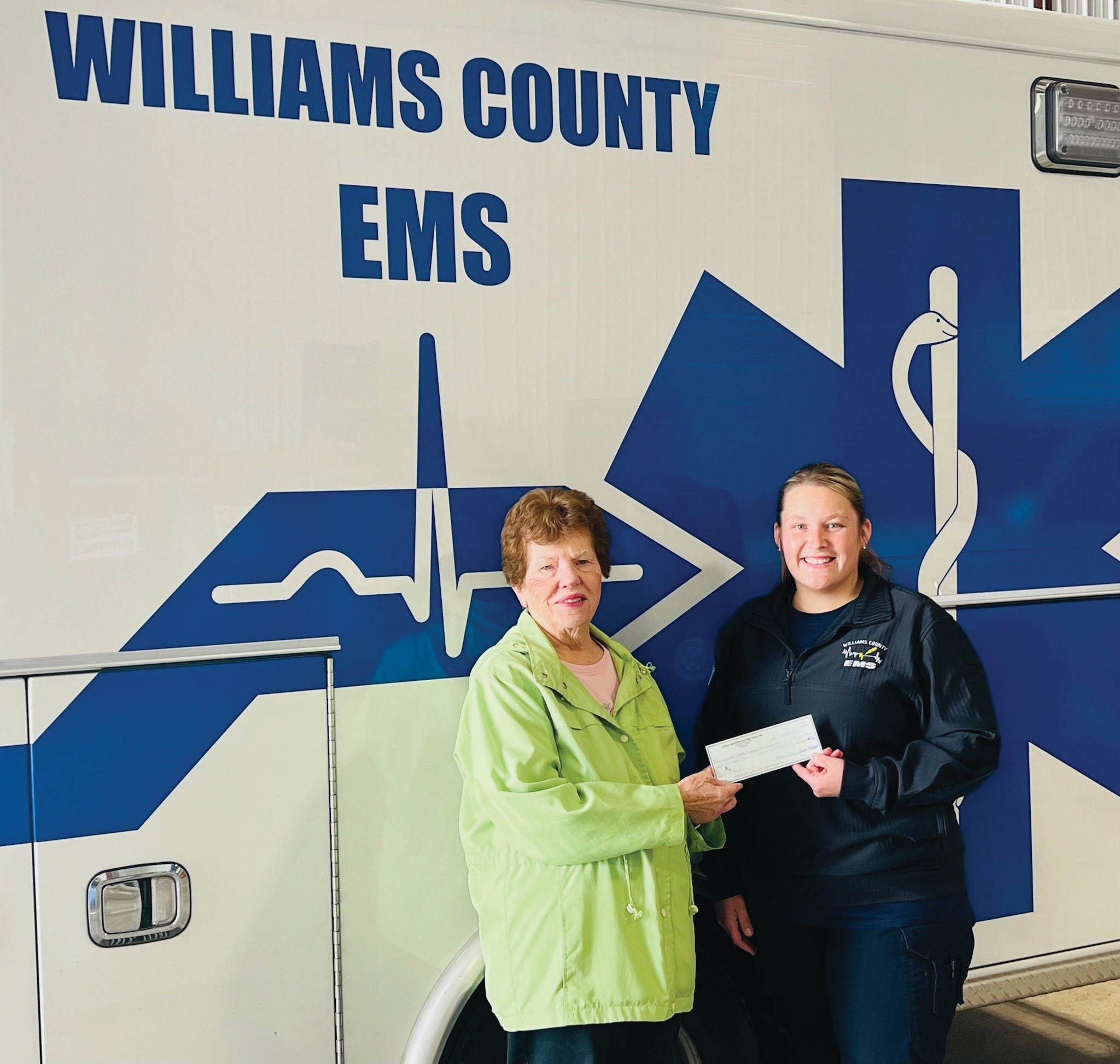 TWO WOMEN STANDING NEXT TO AMBULANCE HOLDING A CHECK