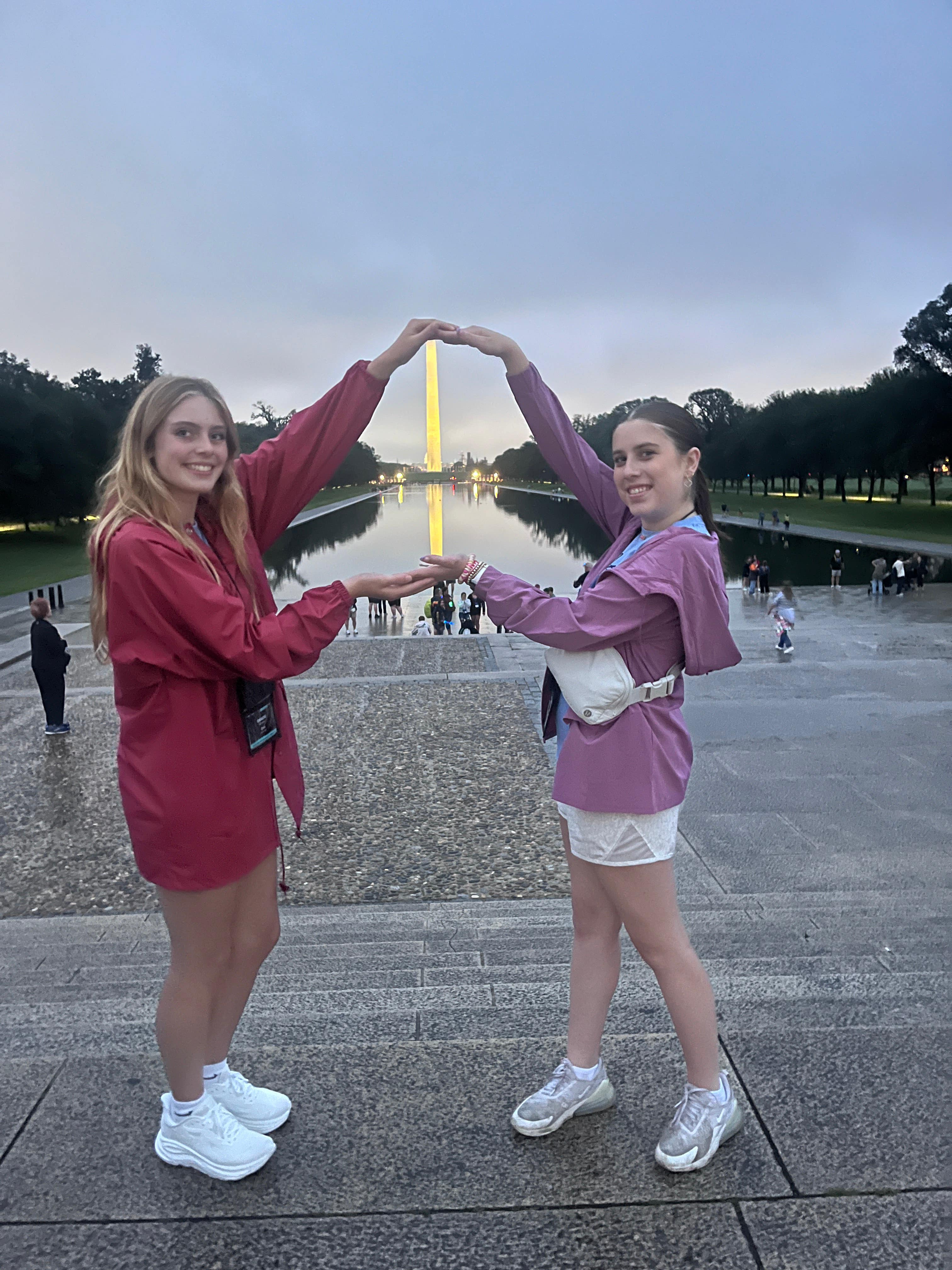 two teenage girls forming a heart with their arms with the monument in the center